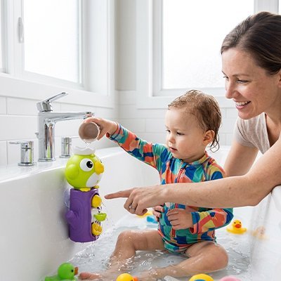 Jouet de bain perroquet à ventouse, coloré, fixé sur le rebord de la baignoire, un enfant souriant joue avec.