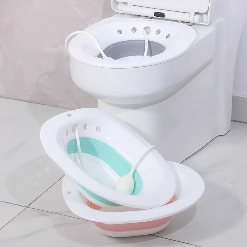 Bain de siège pliable vert pour femme enceinte posé au sol à côté d'un modèle blanc sur les toilettes.
